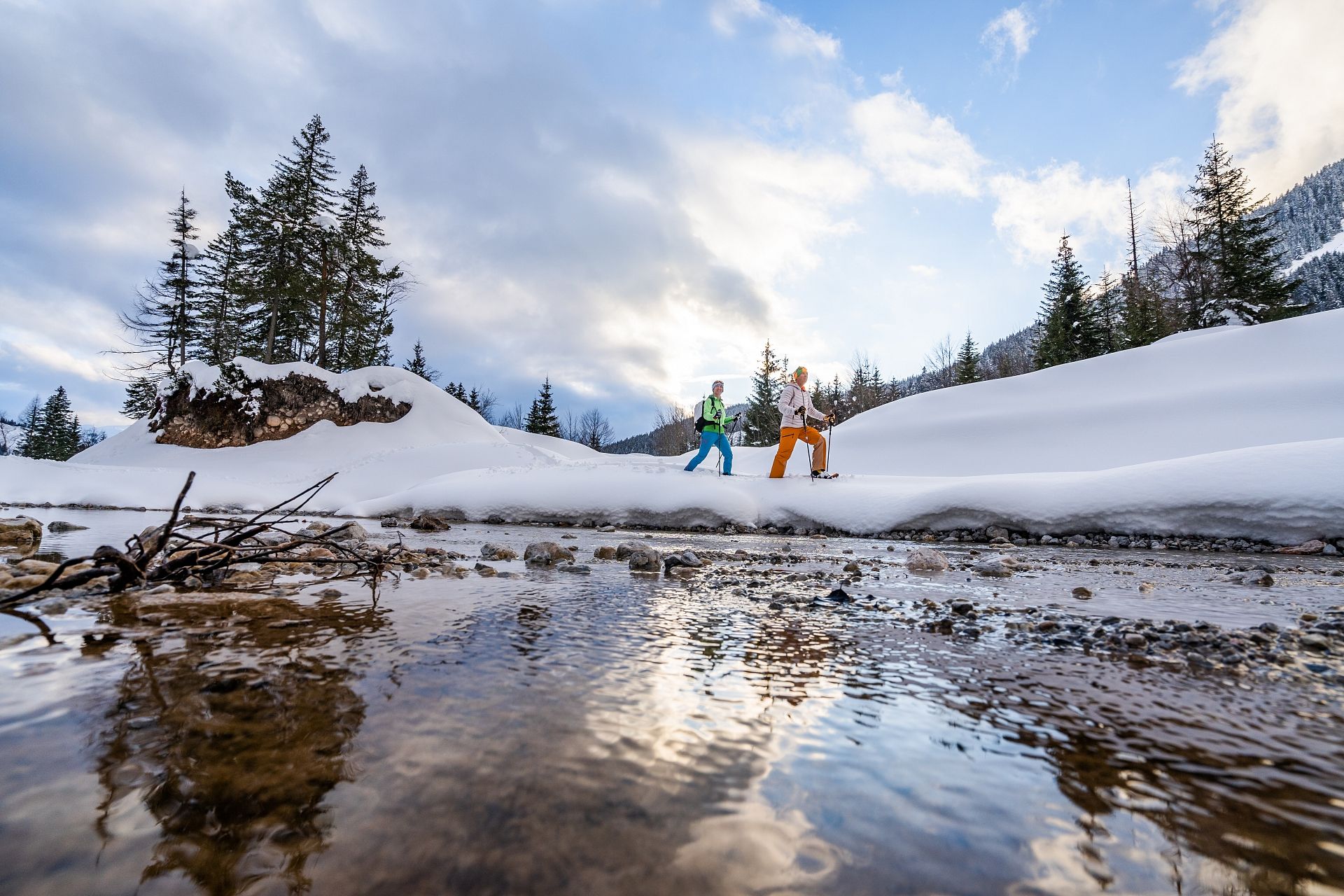 Zwei Schneeschuhwanderer an einem winterlichen Gebirgsbach