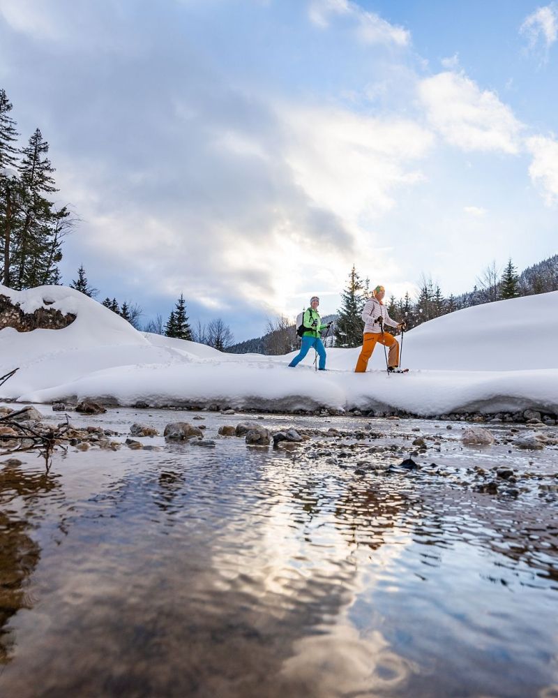 Zwei Schneeschuhwanderer am Bach in der verschneiten Bergwelt