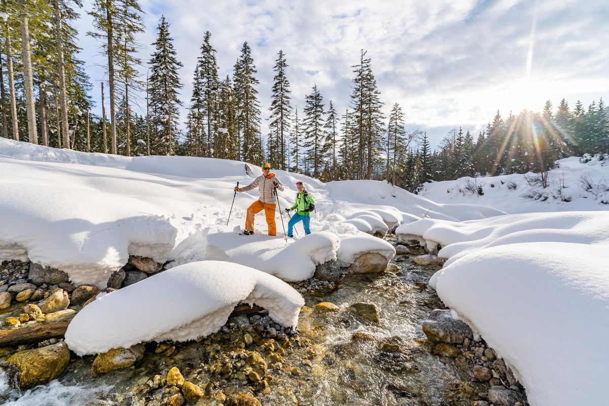 Zwei Schneeschuhwanderer an einem verschneiten Bach