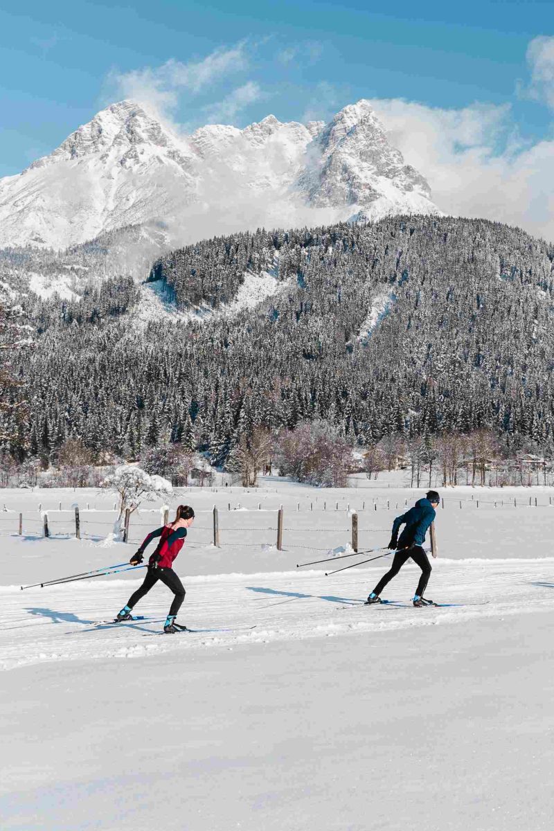 Zwei Langläufer vor einem verschneiten Bergpanorama